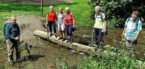 Wandergruppe überquert Bach auf Baumstamm